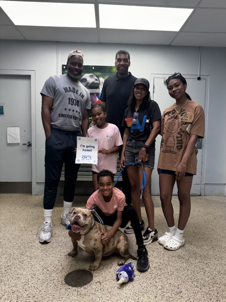 Family of five with a brindle pit bull in the PSPCA lobby holding an 'I'm going home!' sign — adoption day celebration