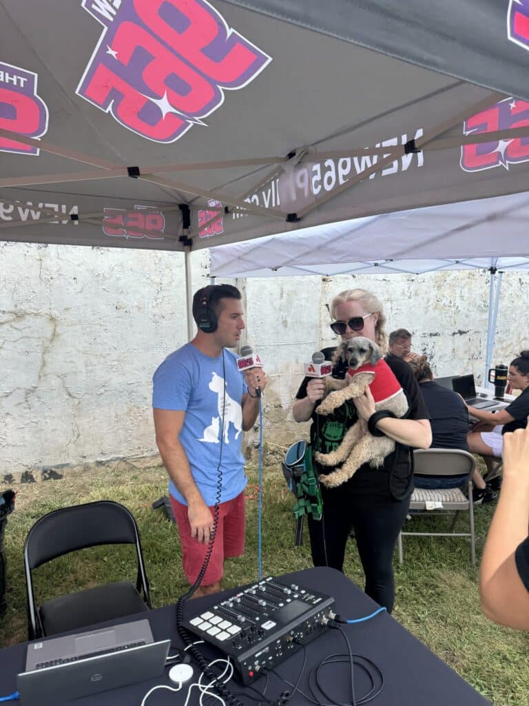 PSPCA staff at a radio station tent with a scruffy dog on someone's lap at a community event